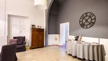 A spacious room with a large clock on the wall, a table with magazines and a bottle, and a cabinet with framed photos.