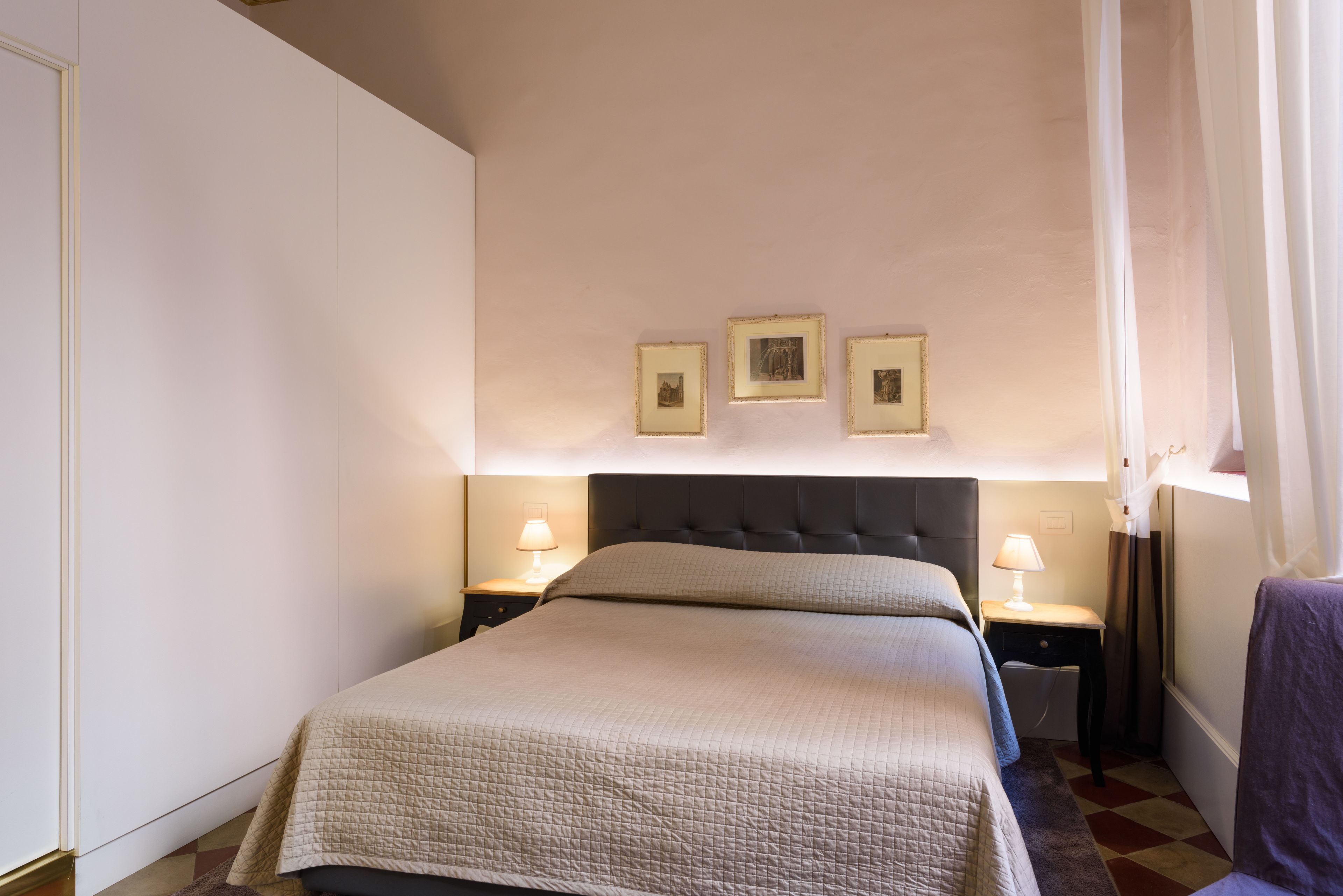 A neatly arranged bedroom with a large bed, bedside tables with lamps, and three framed pictures on the wall.