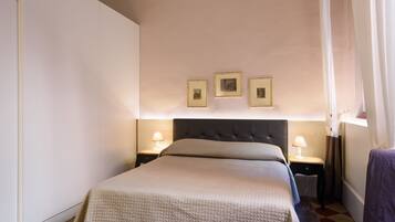 A neatly arranged bedroom with a large bed, bedside tables with lamps, and three framed pictures on the wall.