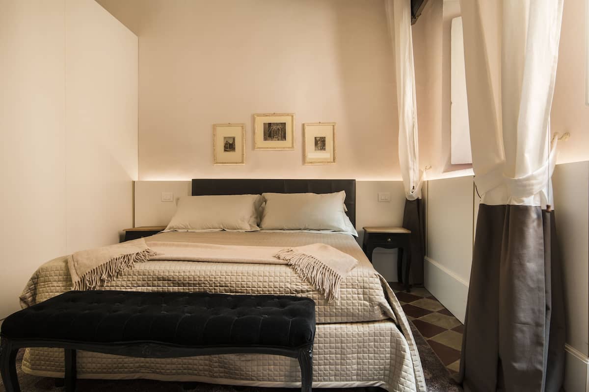 A neatly arranged bedroom with a bed, bedside tables, a bench, and three framed pictures on the wall.