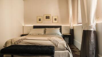 Een netjes ingerichte slaapkamer met een bed, nachtkastjes, een bankje en drie ingelijste foto’s aan de muur.