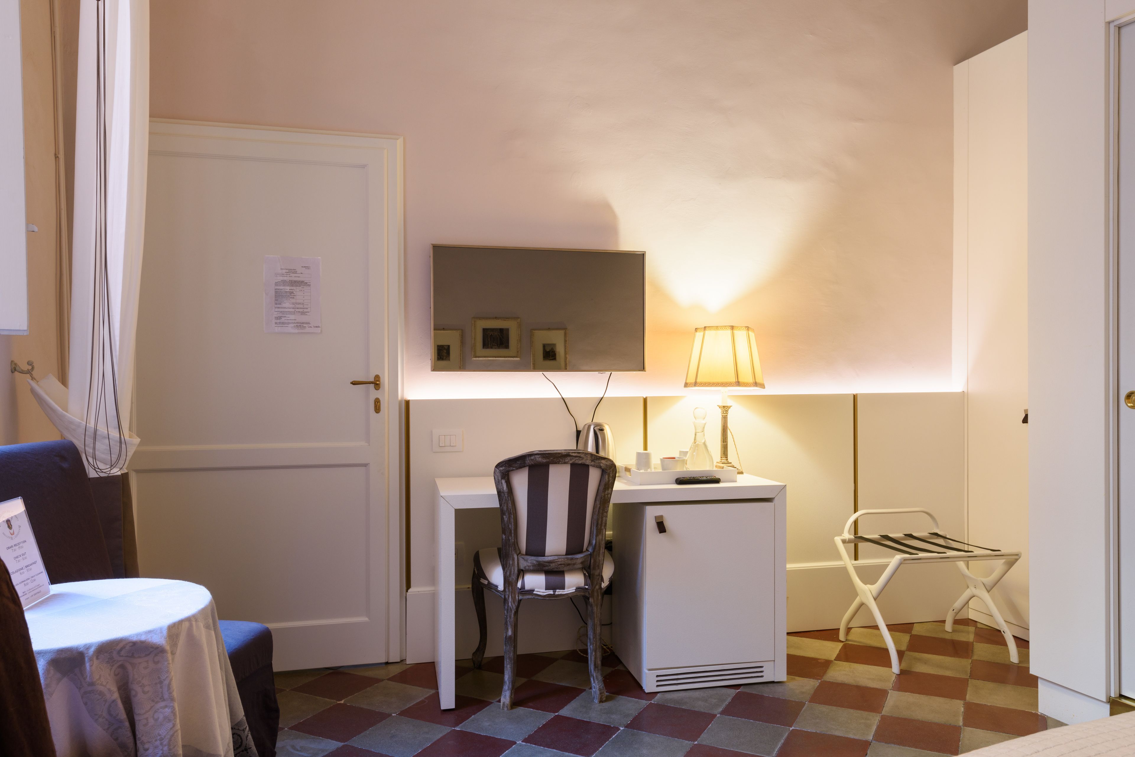Une pièce de taille modeste, équipée d’un bureau, d’une chaise et d’un petit réfrigérateur. Une lampe assure l’éclairage, et on peut apercevoir un étendoir.