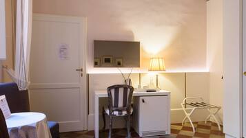 Une pièce de taille modeste, équipée d’un bureau, d’une chaise et d’un petit réfrigérateur. Une lampe assure l’éclairage, et on peut apercevoir un étendoir.