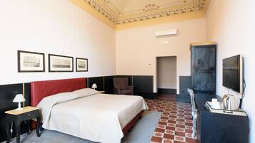 Habitació d'hotel amb un llit gran, una escriptori amb una làmpada, una cadira, un televisor i una nevera petit.