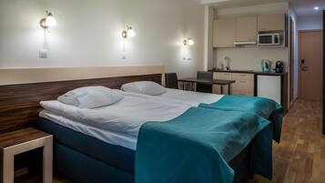 Habitación de hotel con cama, mesita de noche y zona de kitchenette.