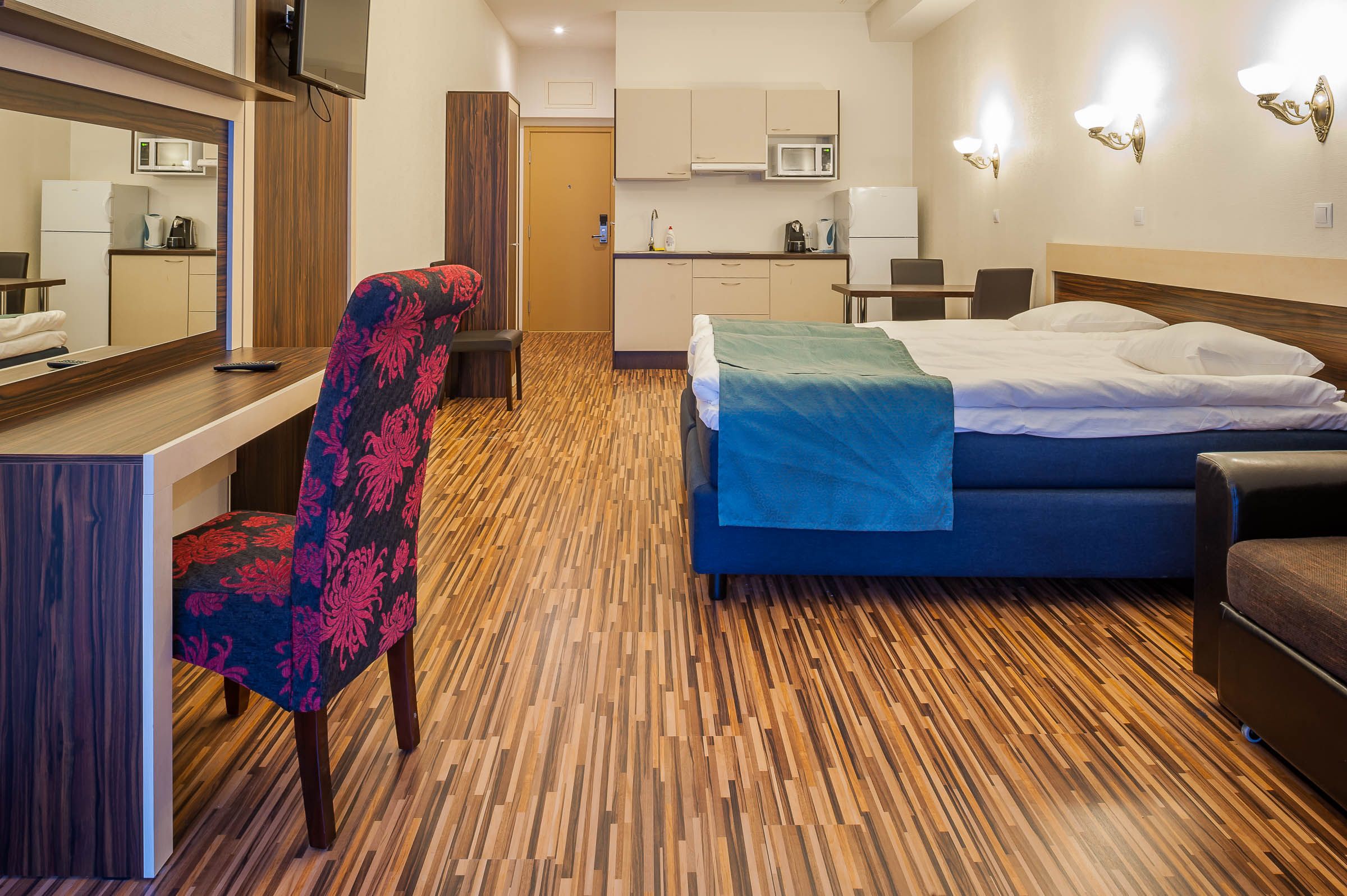 A hotel room with a bed, a desk, a chair, a microwave, and a kitchenette.