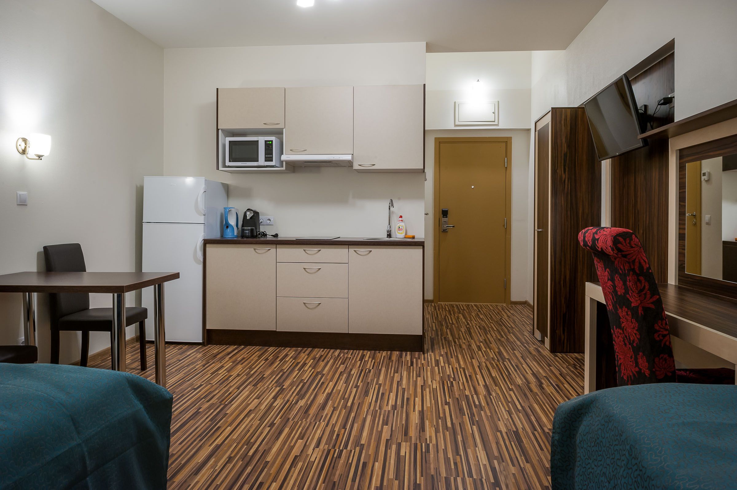 Habitación de hotel pequeña con kitchenette, comedor y cama.