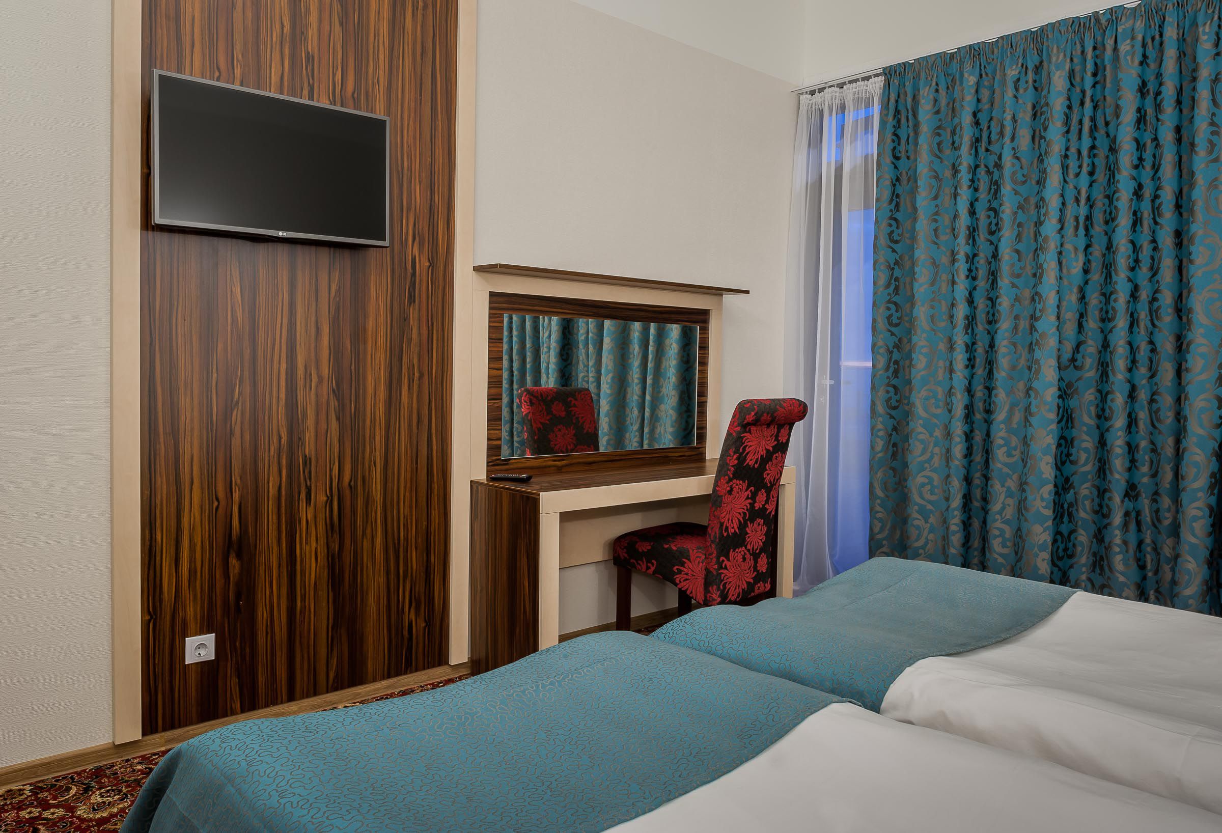 Une chambre d’hôtel comprenant un lit, un bureau avec une chaise, un téléviseur fixé au mur et une fenêtre avec des rideaux.