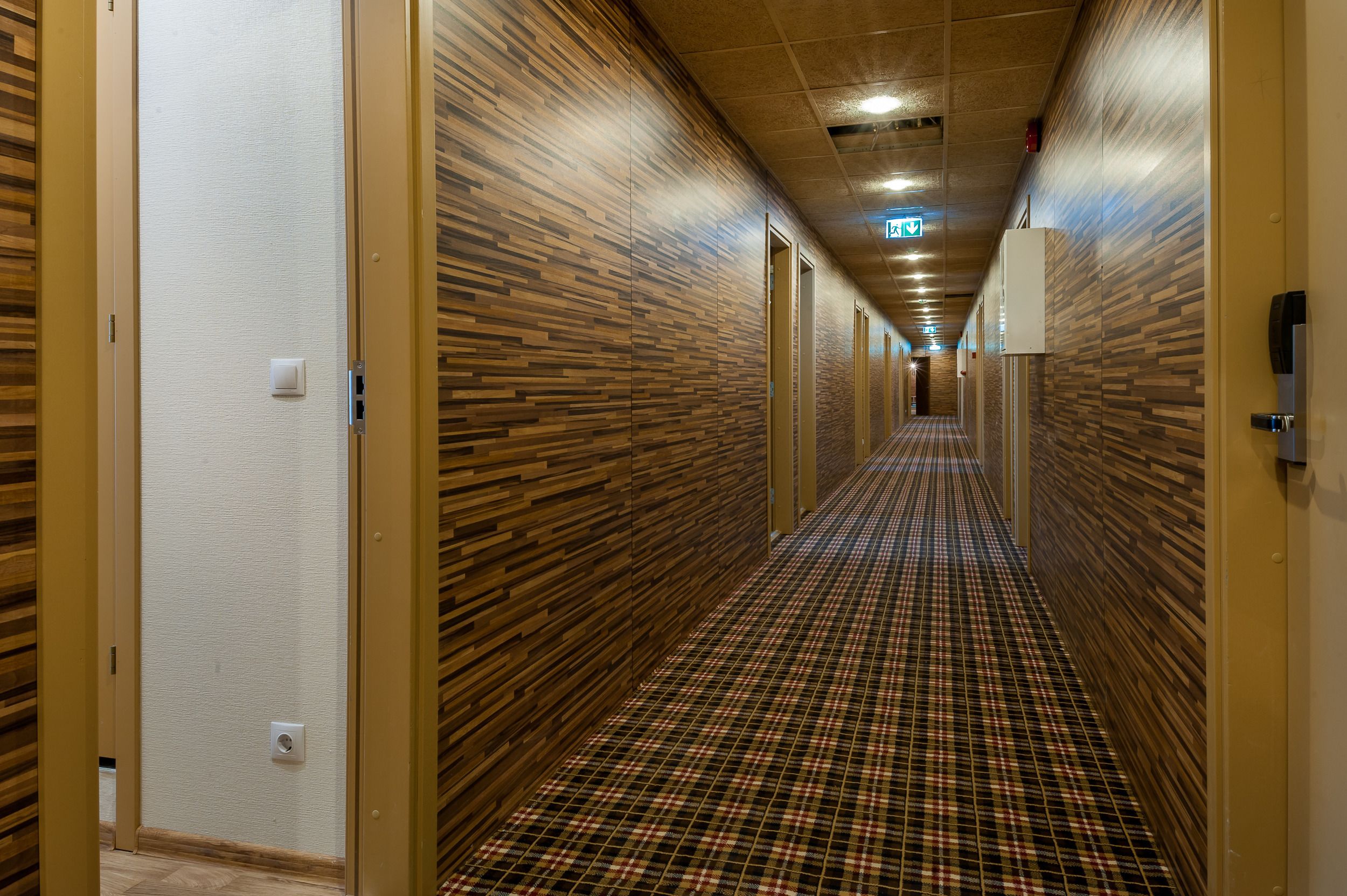Ein Hotelkorridor mit Holzwandverkleidung, einem Schachbrettmuster-Boden und Türen auf beiden Seiten.