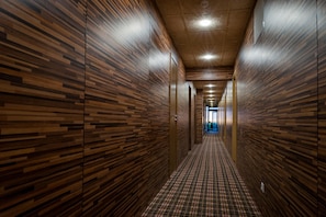 Ein Korridor mit Holzwandverkleidung und einem Schachbrettmuster-Boden, der zu einer Tür am Ende führt.