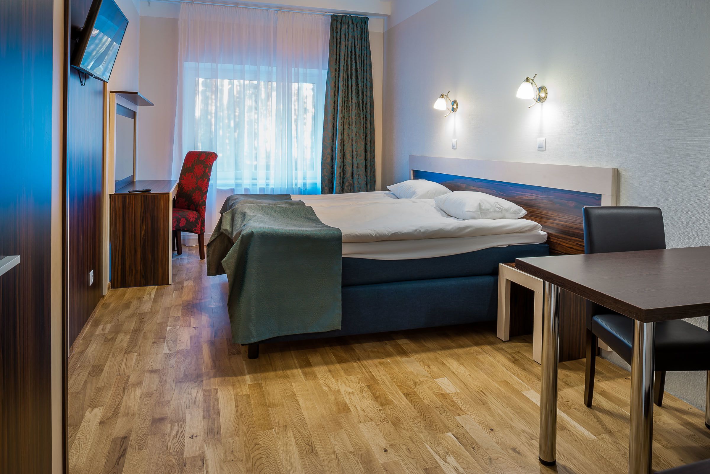 A hotel room with a bed, a desk, a chair, a TV, and a window with curtains.
