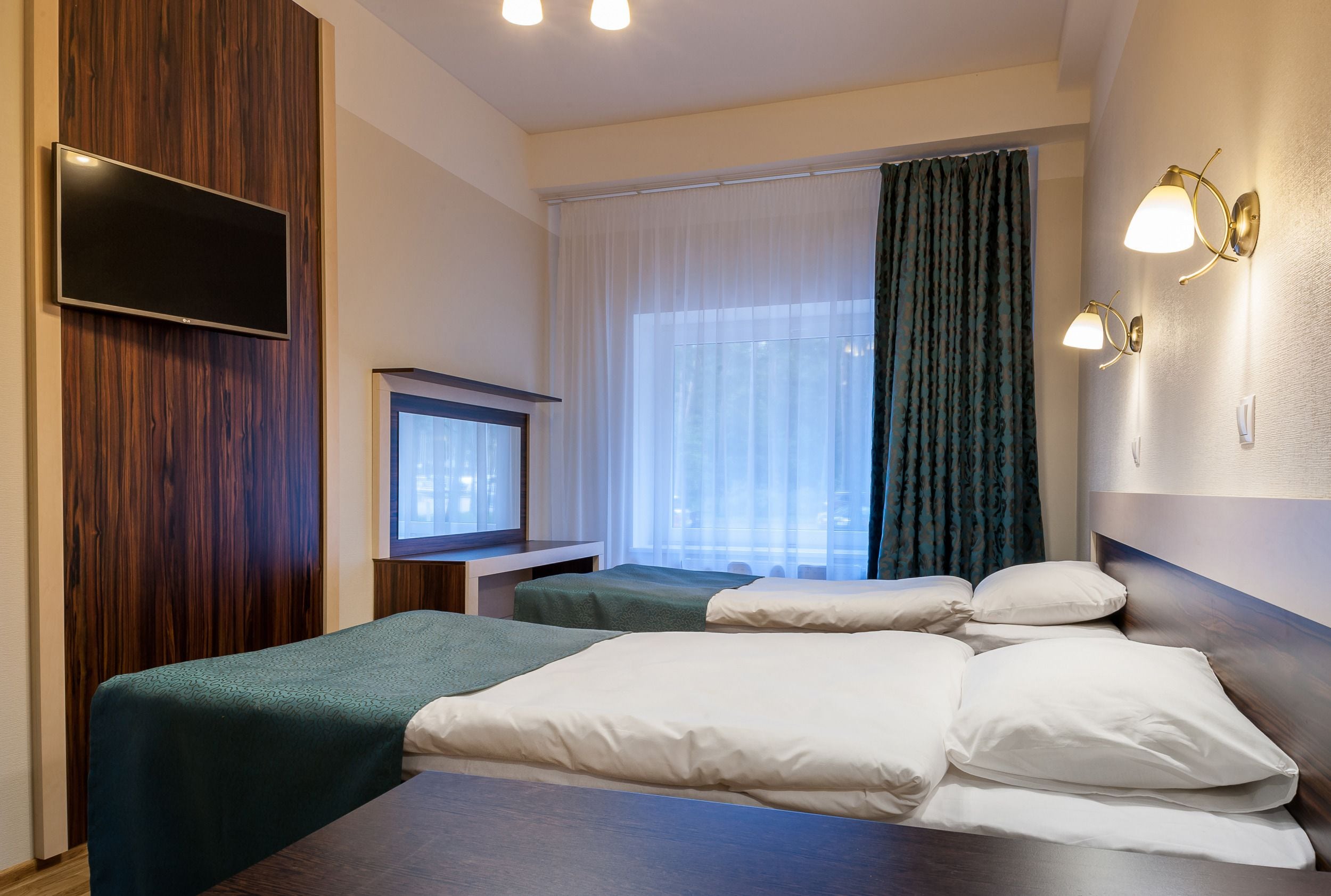 Ein Hotelzimmer mit zwei Betten, einem Fernseher und einem Fenster mit Vorhängen.