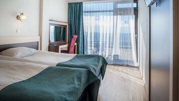 A hotel room with two beds, a desk, a chair, a TV, and a balcony with a view.
