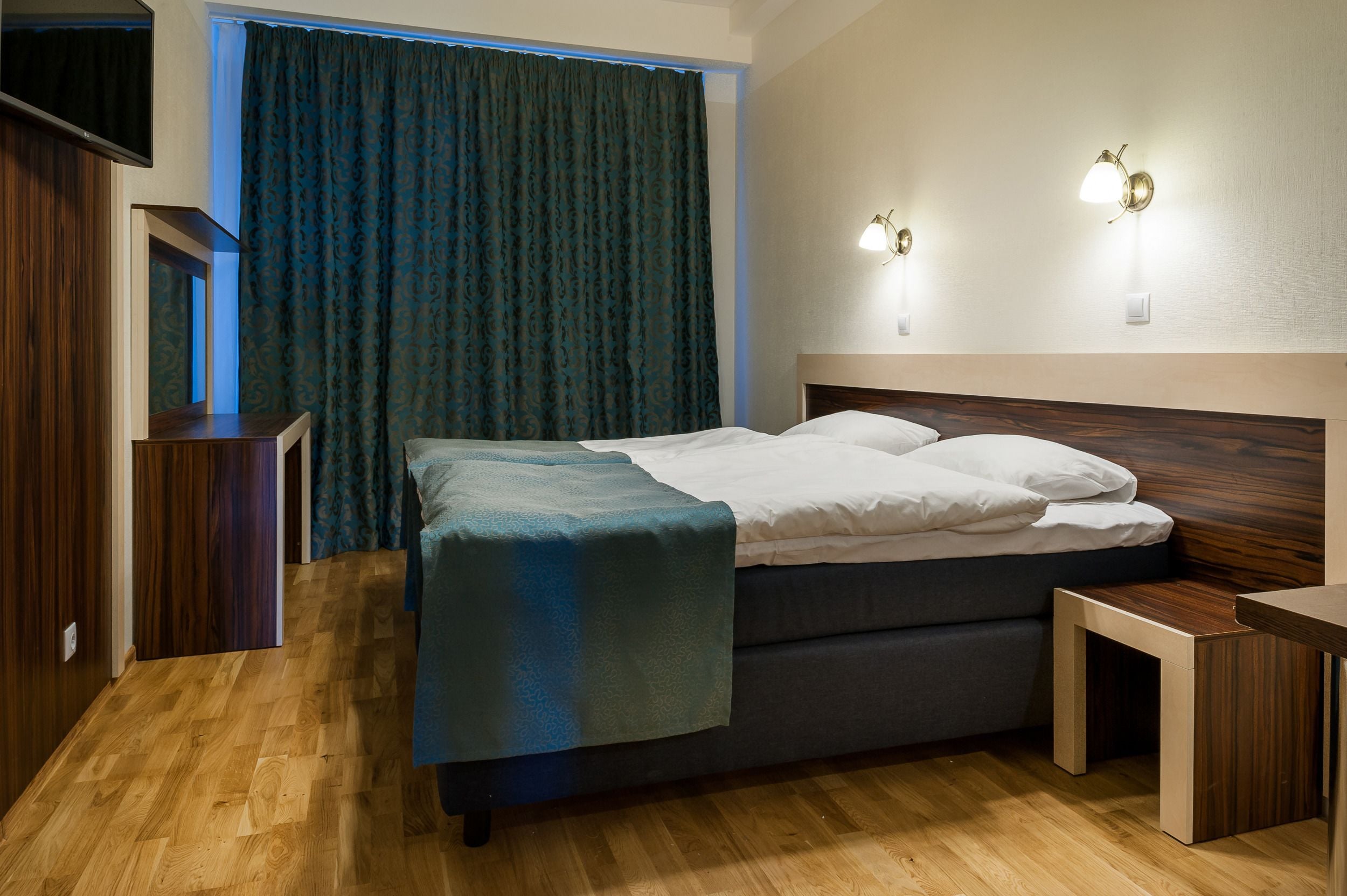 A neatly arranged bedroom with a bed, bedside tables, and a TV mounted on the wall.