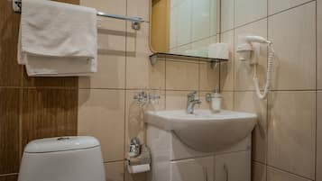 A bathroom with a toilet, sink, towel rack, and a hairdryer on a shelf.