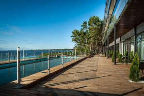 A wooden deck with a pool, overlooking the sea, and a building with outdoor seating. - Pirita Beach Apartments & SPA (Tallinn)