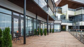 A modern building with a wooden deck, outdoor seating, and large windows.