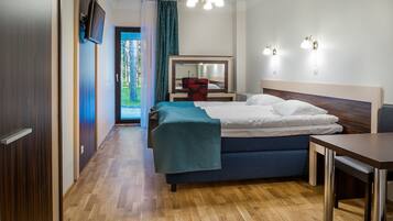 A hotel room with a bed, a desk, a chair, a TV mounted on the wall, and a mirror above the bed.