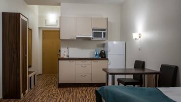 A compact hotel room with a kitchenette, a bed, a small table, and a chair.