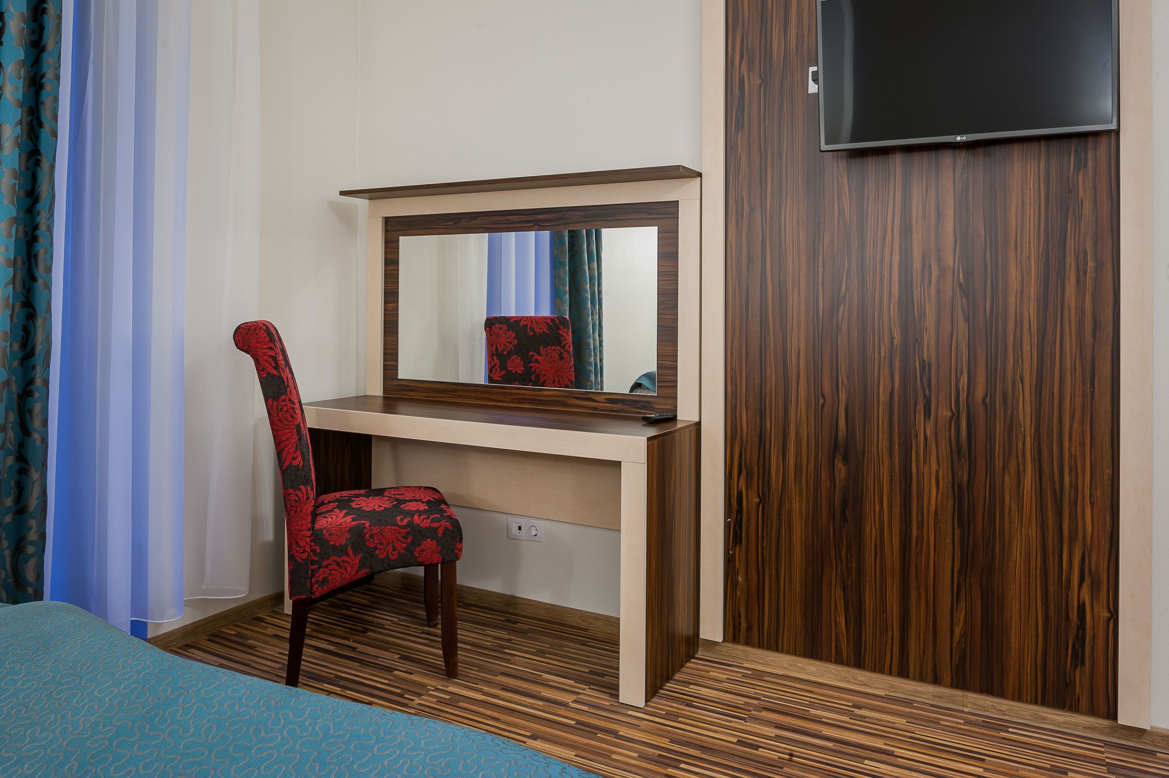 Une chambre d’hôtel avec un bureau en bois, une chaise, un lit recouvert d’une courtepointe à motifs bleus et un téléviseur fixé au mur.