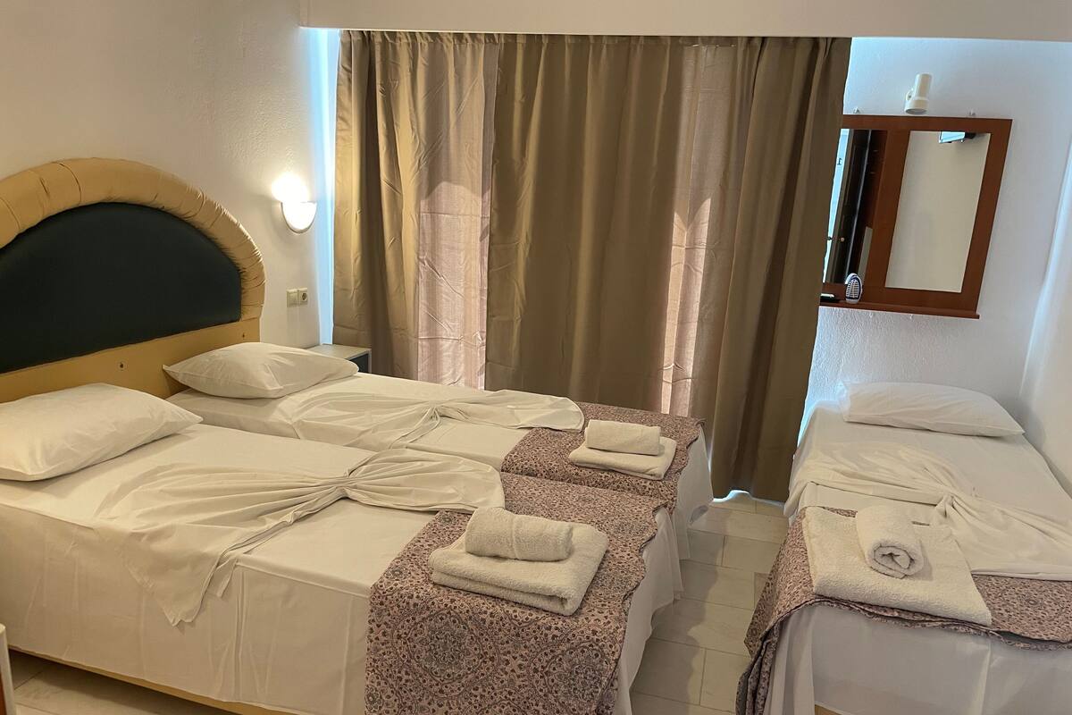 Een hotelkamer met twee bedden, elk voorzien van witte lakens en handdoeken, een hoofdbord, een nachtkastje en een spiegel aan de muur.