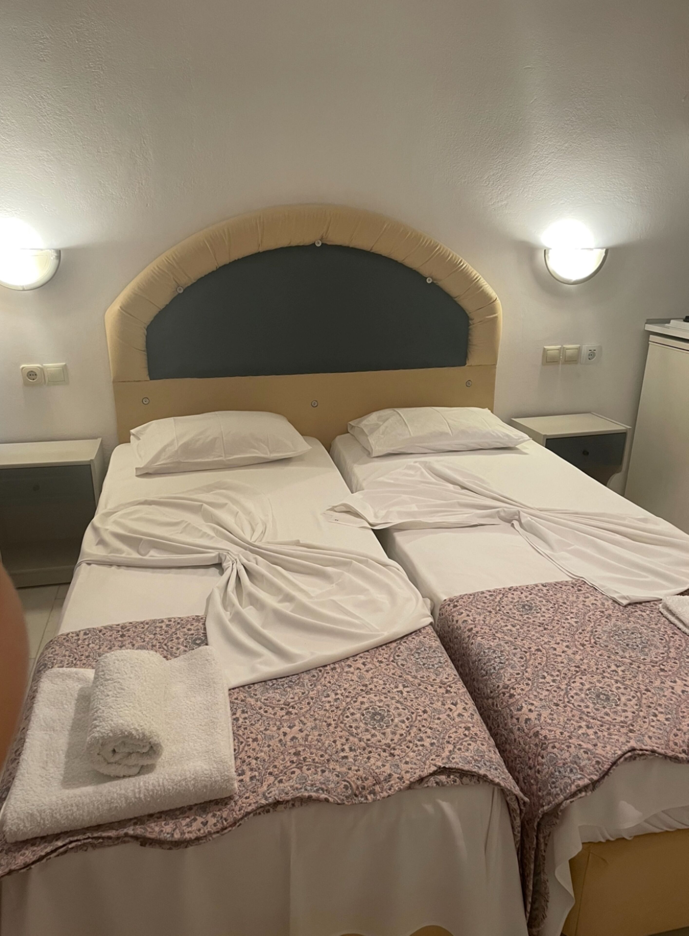 Een tweepersoonsbed met hoofdeinde, twee nachtkastjes en een wandlamp.