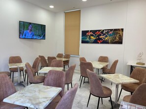 A conference room with marble tables and cushioned chairs, a TV screen, and two artworks on the walls. - Hotel Kourkoumelata (Kefalonia)