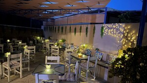 An outdoor dining area with tables and chairs, string lights, and hanging plants. - Hotel Kourkoumelata (Kefalonia)