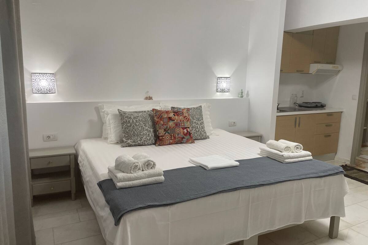 Een keurig opgemaakt hotelkamer met een bed, kussens, een nachtkastje, een klein bureau en een inbouwkast.