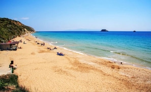 A beach with a sandy shore, a few people, and a small island in the distance. - Hotel Kourkoumelata (Kefalonia)