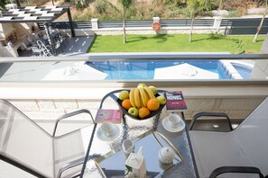 Un balcón con vista a la piscina, una mesa con fruta, un libro y un cartel.