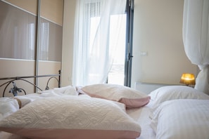 A bedroom with a bed, a bedside table with a lamp, and a window with sheer curtains.