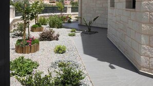 Un edificio moderno con fachada de piedra, un balcón y un jardín con plantas y una pequeña fuente.