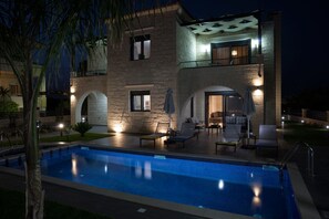 A two-story stone building with a swimming pool, outdoor seating, and a covered patio area.