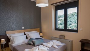 Una cama bien hecha con almohadas blancas y azules, una lámpara de noche y vistas a la vegetación a través de una ventana.