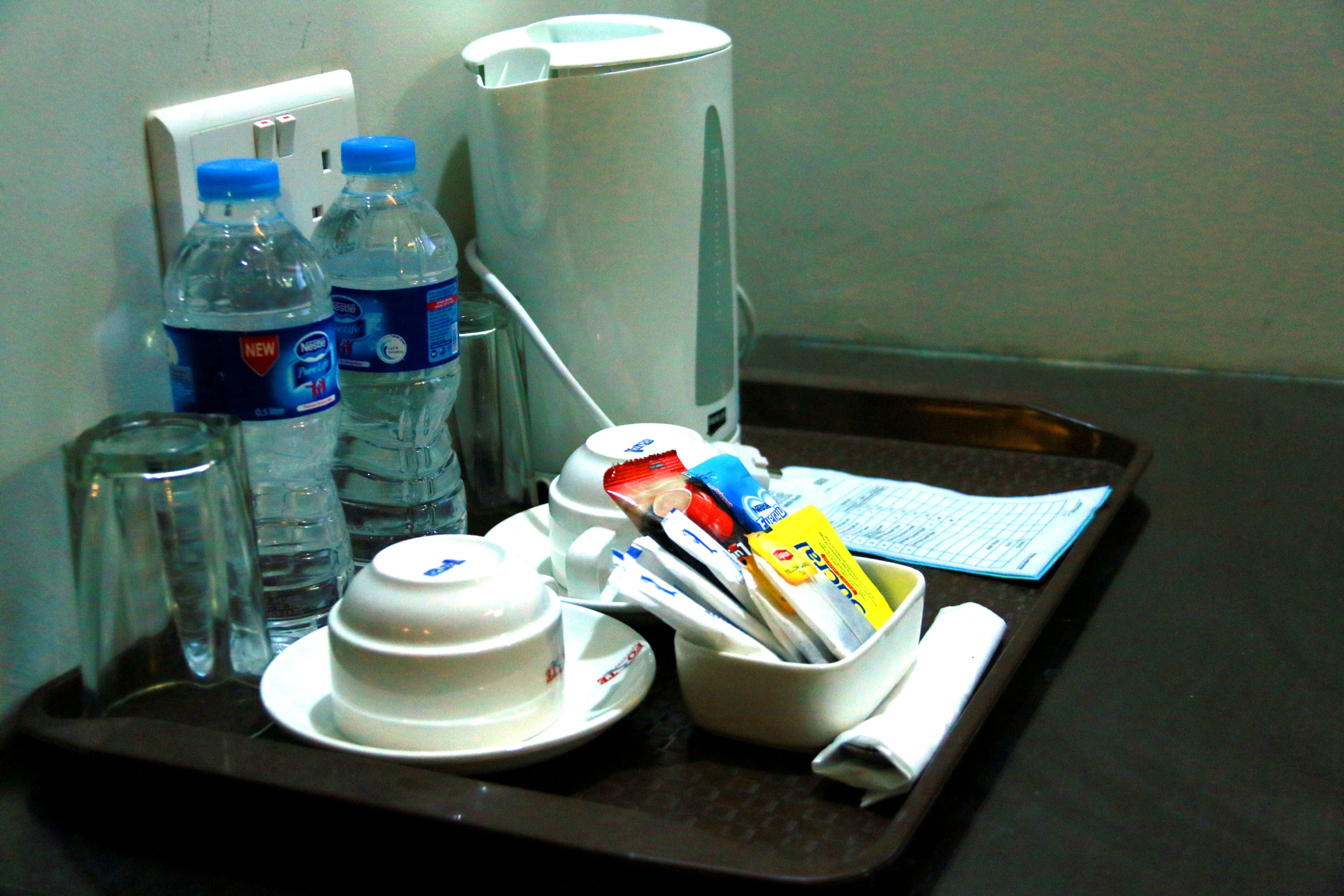 Una bandeja con cafetera, dos botellas de agua, un vaso, un bol y algunos artículos de aseo.