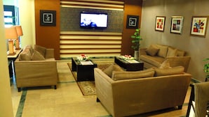 A hotel lobby with a sofa set, a coffee table, a TV mounted on the wall, and framed pictures on the wall. - Hotel One Abbottabad (Abbottabad)