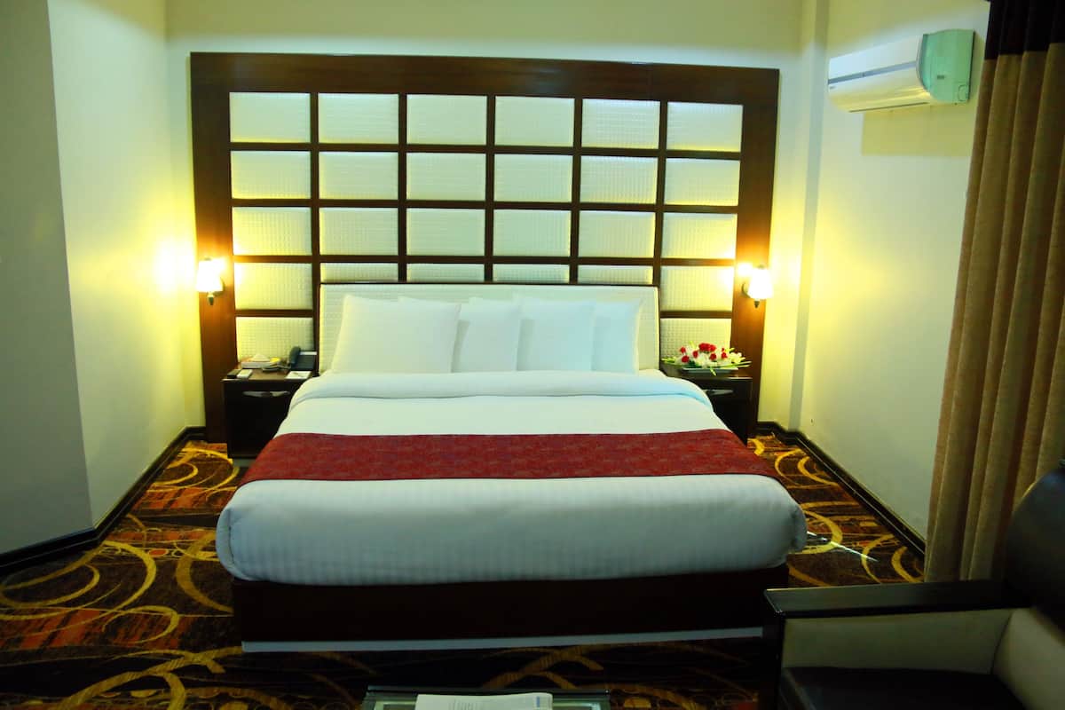 Una habitación de hotel con una cama grande, dos mesitas de noche, una lámpara de noche, una manta roja y un aire acondicionado de pared.