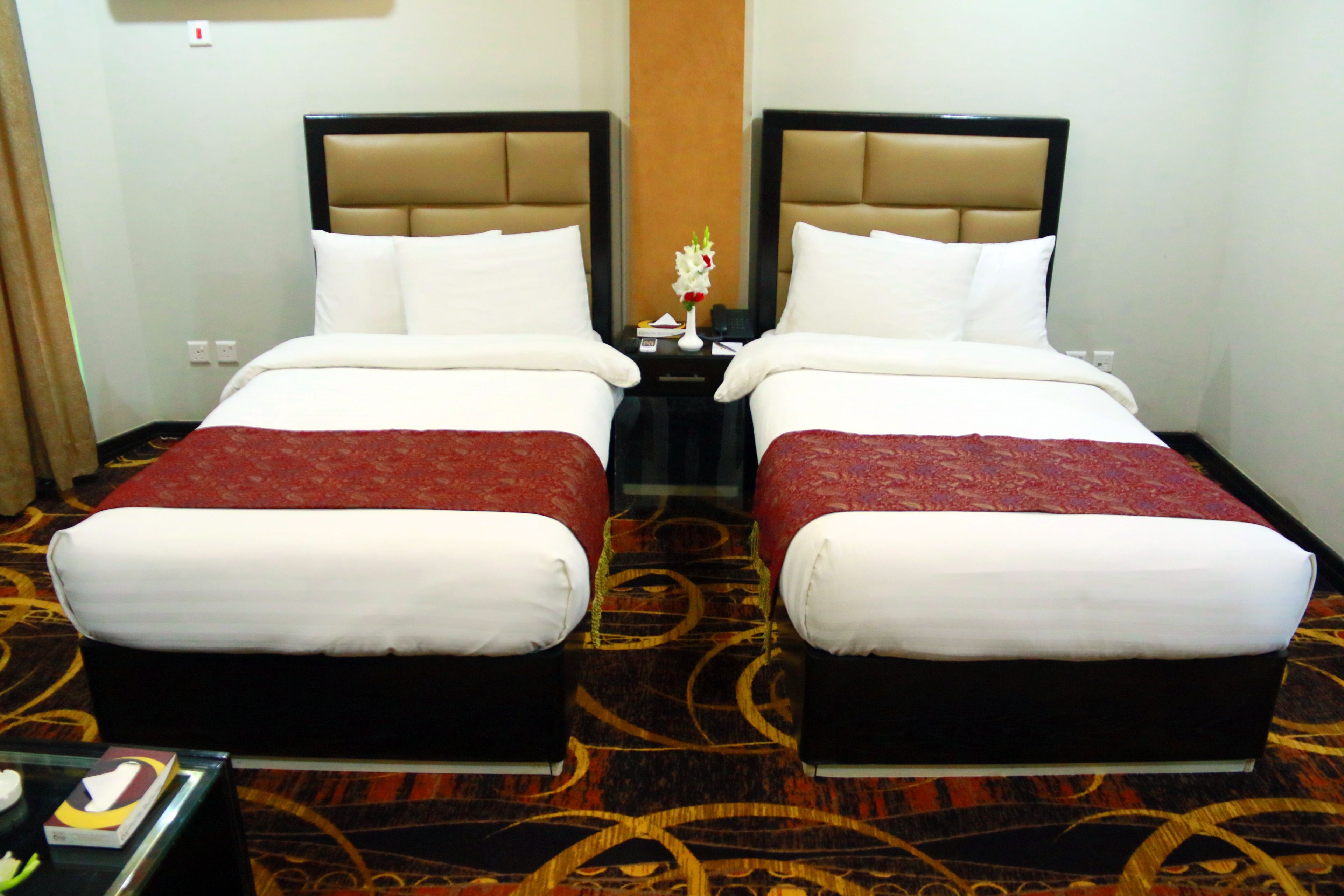 A hotel room with two beds, a nightstand, and a small table with a vase of flowers.