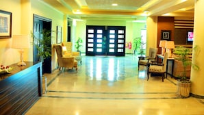 A hotel lobby with a reception desk, seating area, and a large door. - Hotel One Abbottabad (Abbottabad)