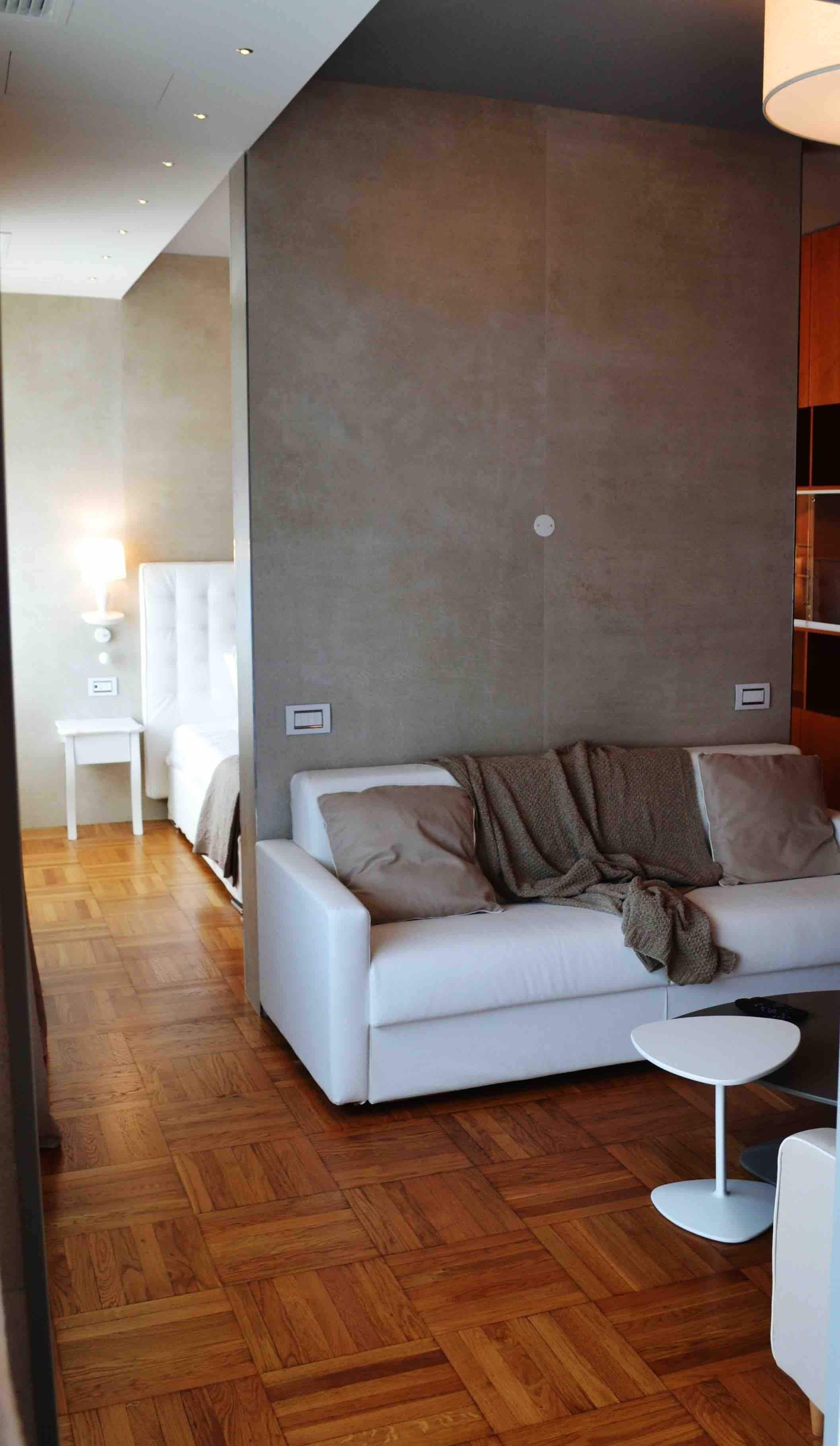 Quarto de hotel moderno com sofá branco, uma mesa redonda pequena e cama com cabeceira.
