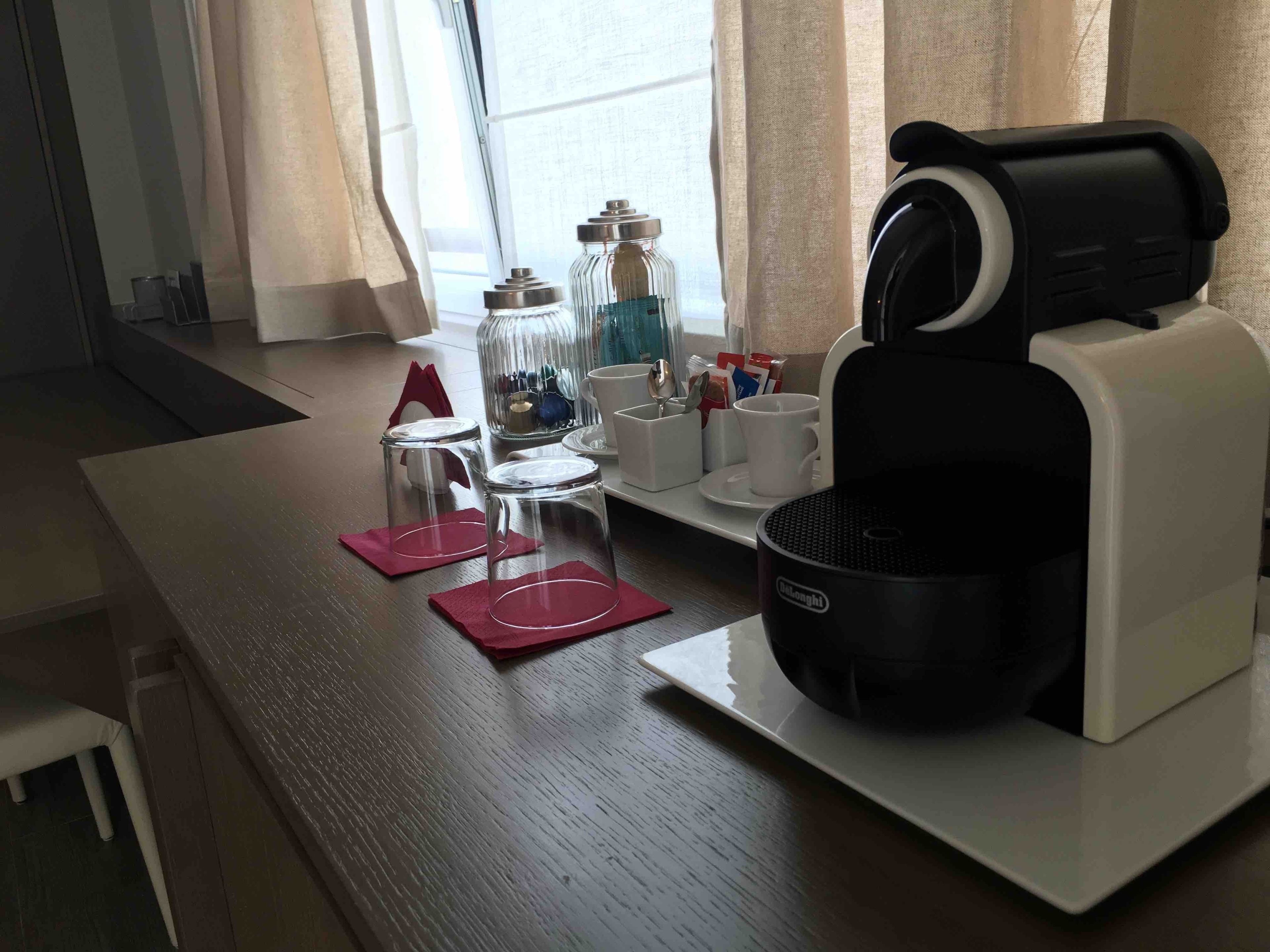 Una estación de café con cafetera, tazas y un recipiente para azúcar sobre una mesa.