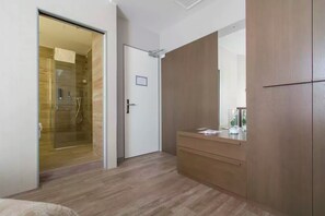 A modern bedroom with a wooden floor, a glass shower enclosure, a wooden wardrobe, and a bedside table with a mirror. - Ginevra Rooms Bergamo (Bergamo)