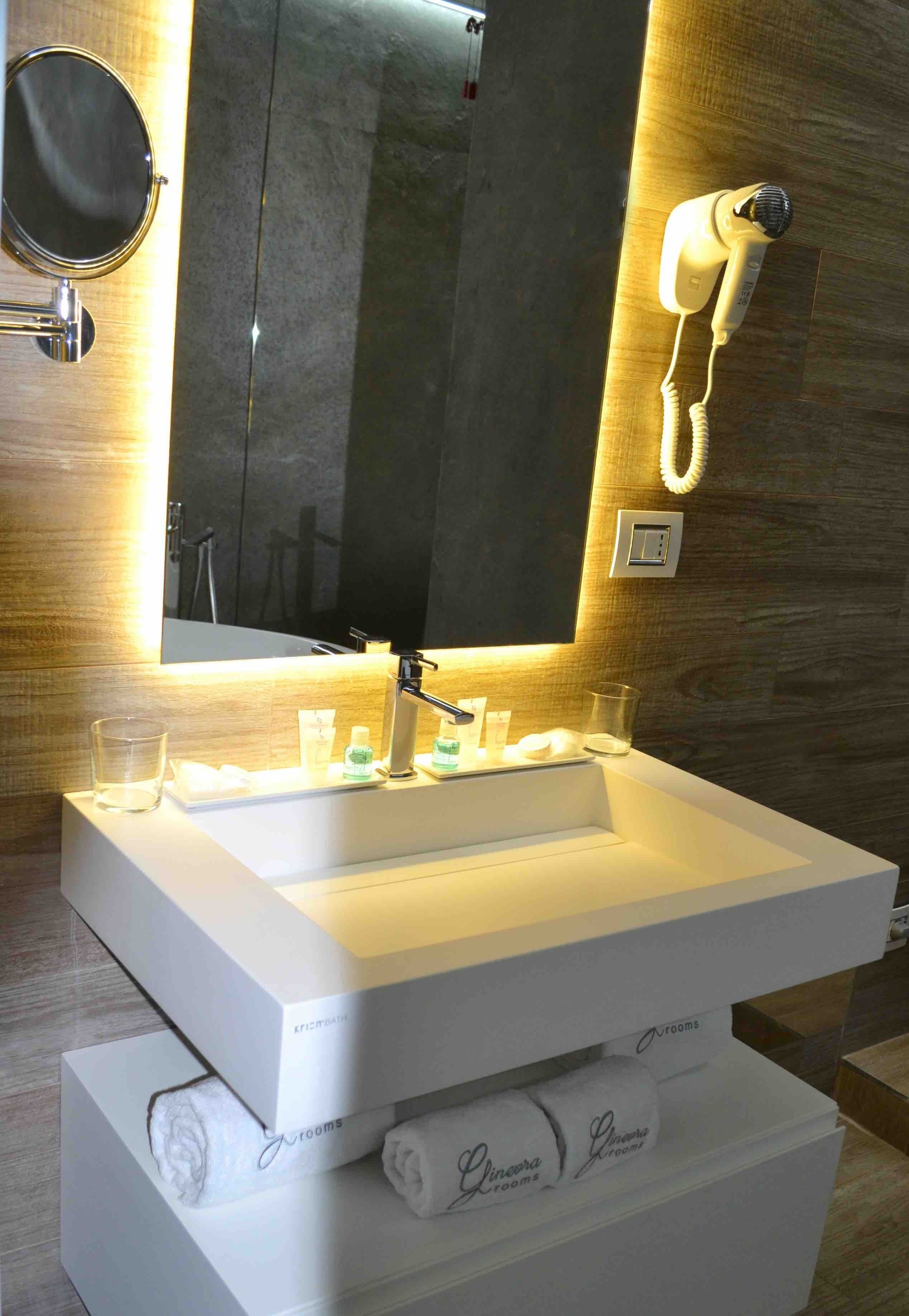 Une salle de bain moderne avec un grand miroir, un lavabo blanc, un sèche-cheveux et des articles de toilette posés sur le comptoir.