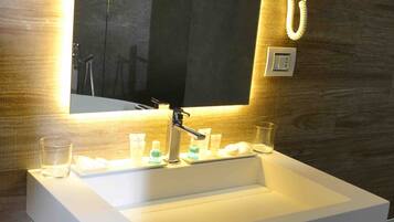 Une salle de bain moderne avec un grand miroir, un lavabo blanc, un sèche-cheveux et des articles de toilette posés sur le comptoir.