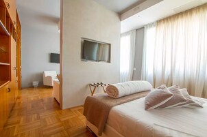 Una camera d'albergo con un letto, una TV a muro, un armadio in legno e una finestra con tende.