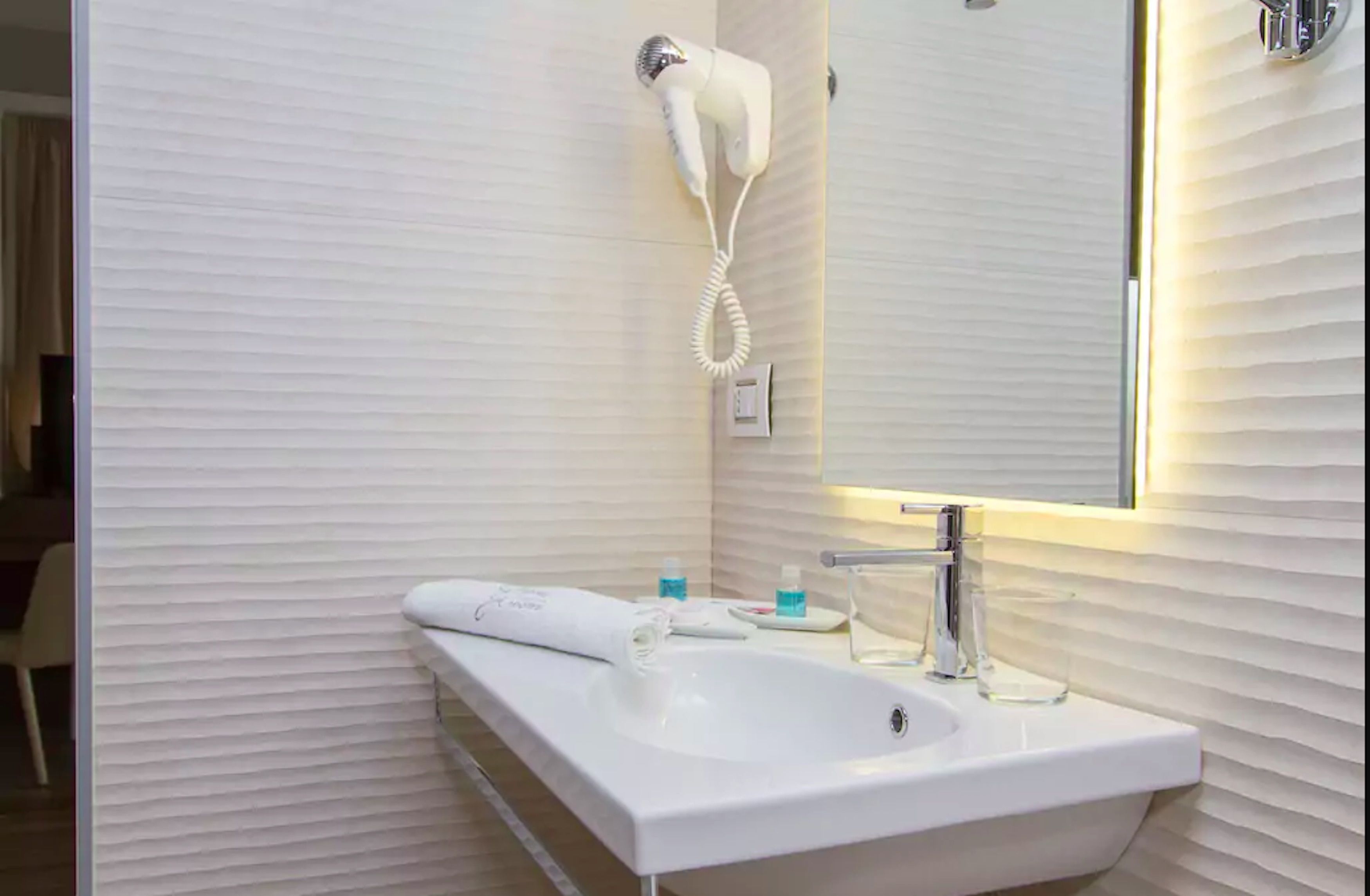 A bathroom with a white sink, a hairdryer mounted on the wall, a mirror, and a towel.