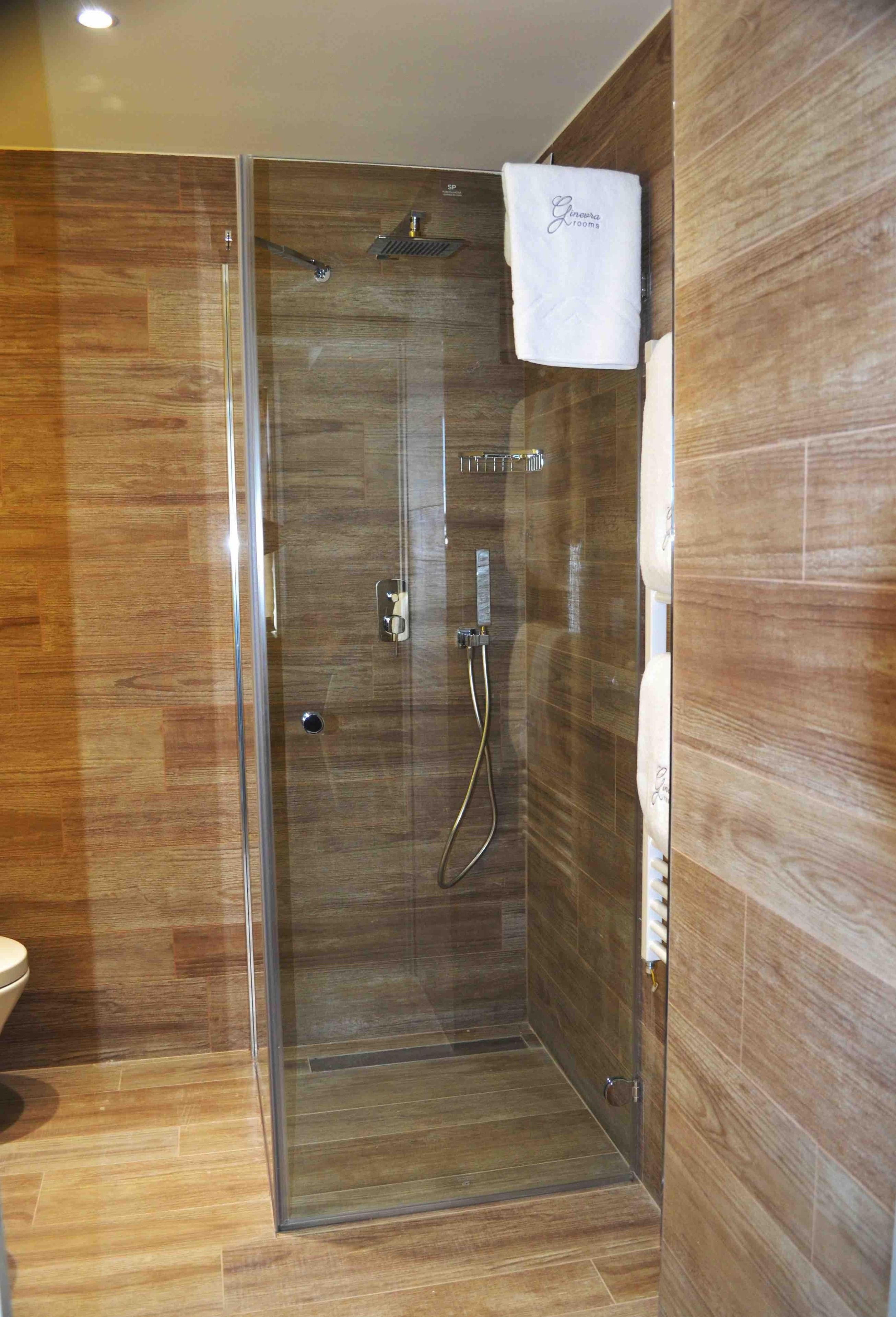 A glass-enclosed shower with a wooden floor and a towel hanging on the wall.
