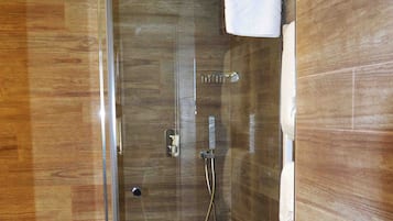 A glass-enclosed shower with a wooden floor and a towel hanging on the wall.