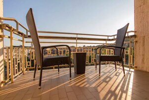Un balcone con due poltrone in vimini e un tavolino, vista sulla città.